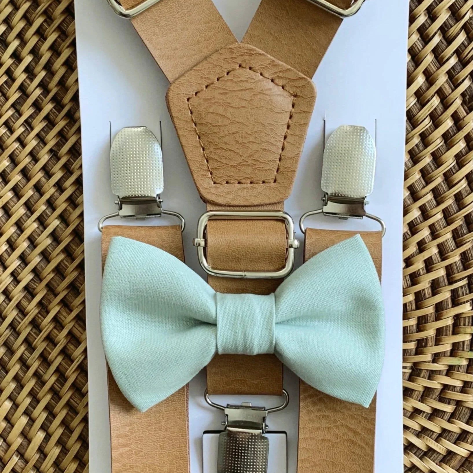 Tan vegan leather suspenders with sage bow tie displayed on a white card against a woven surface