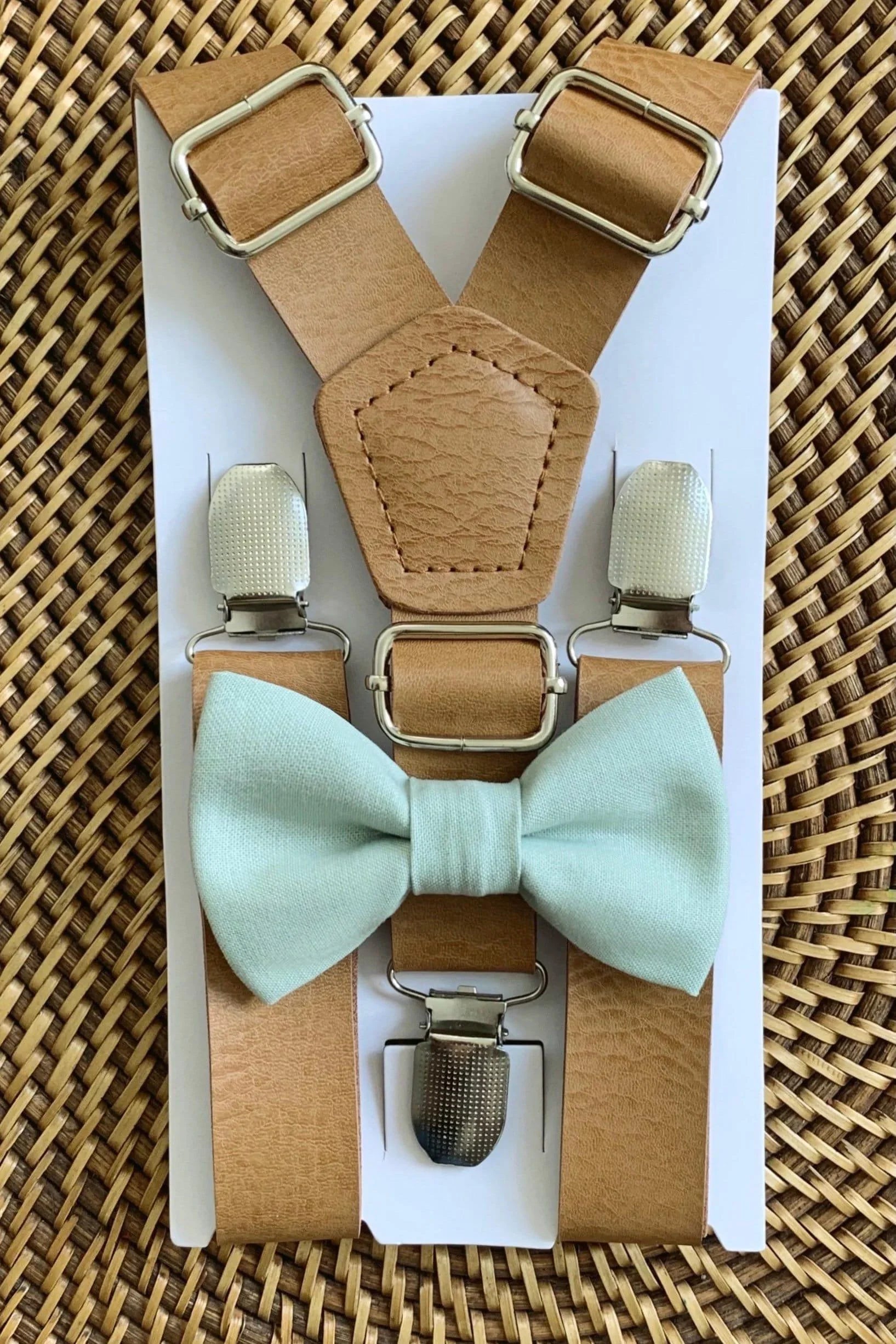 Tan vegan leather suspenders with sage bow tie displayed on a white card against a woven surface