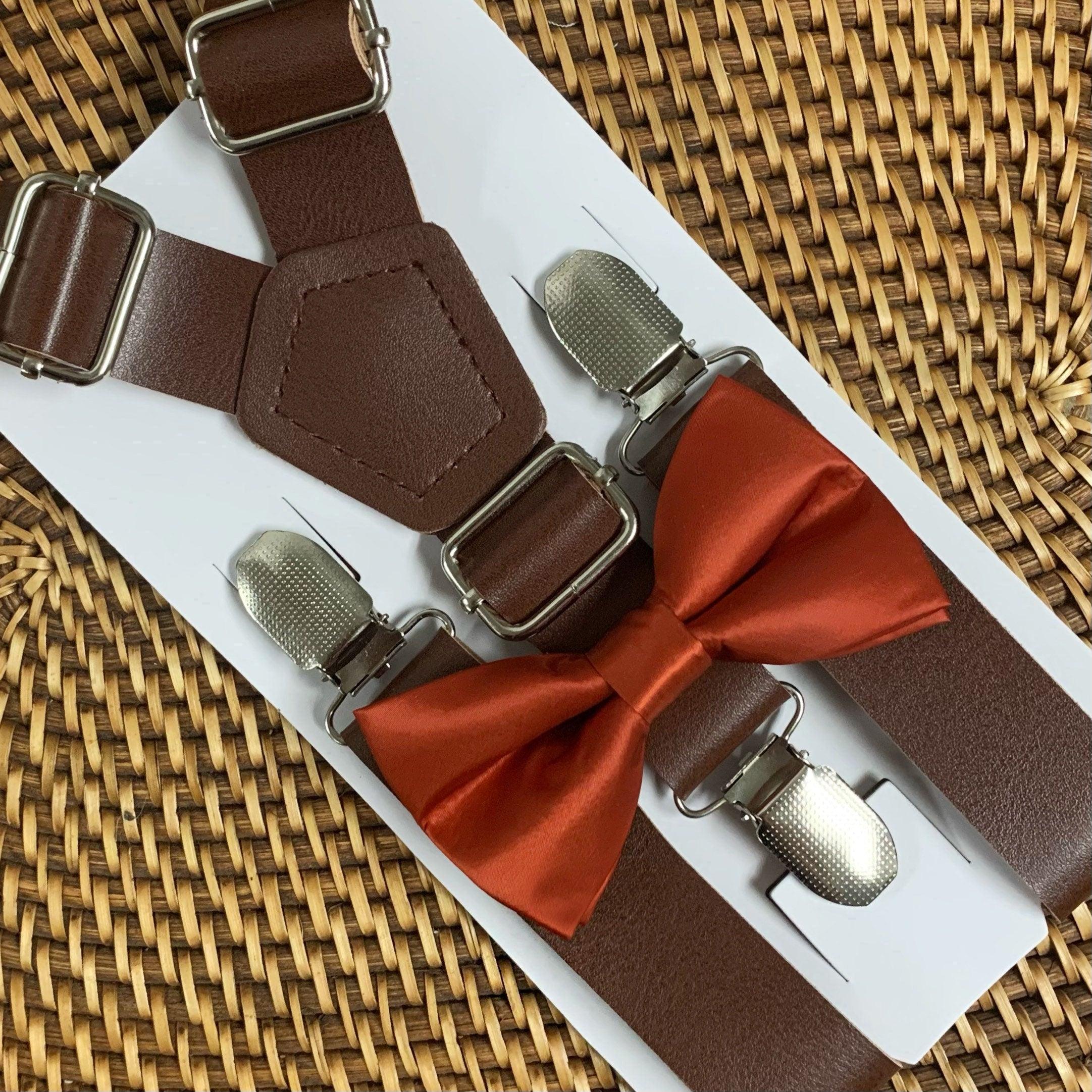 A set of burnt orange bow tie and dark vegan leather suspenders displayed on a white background.