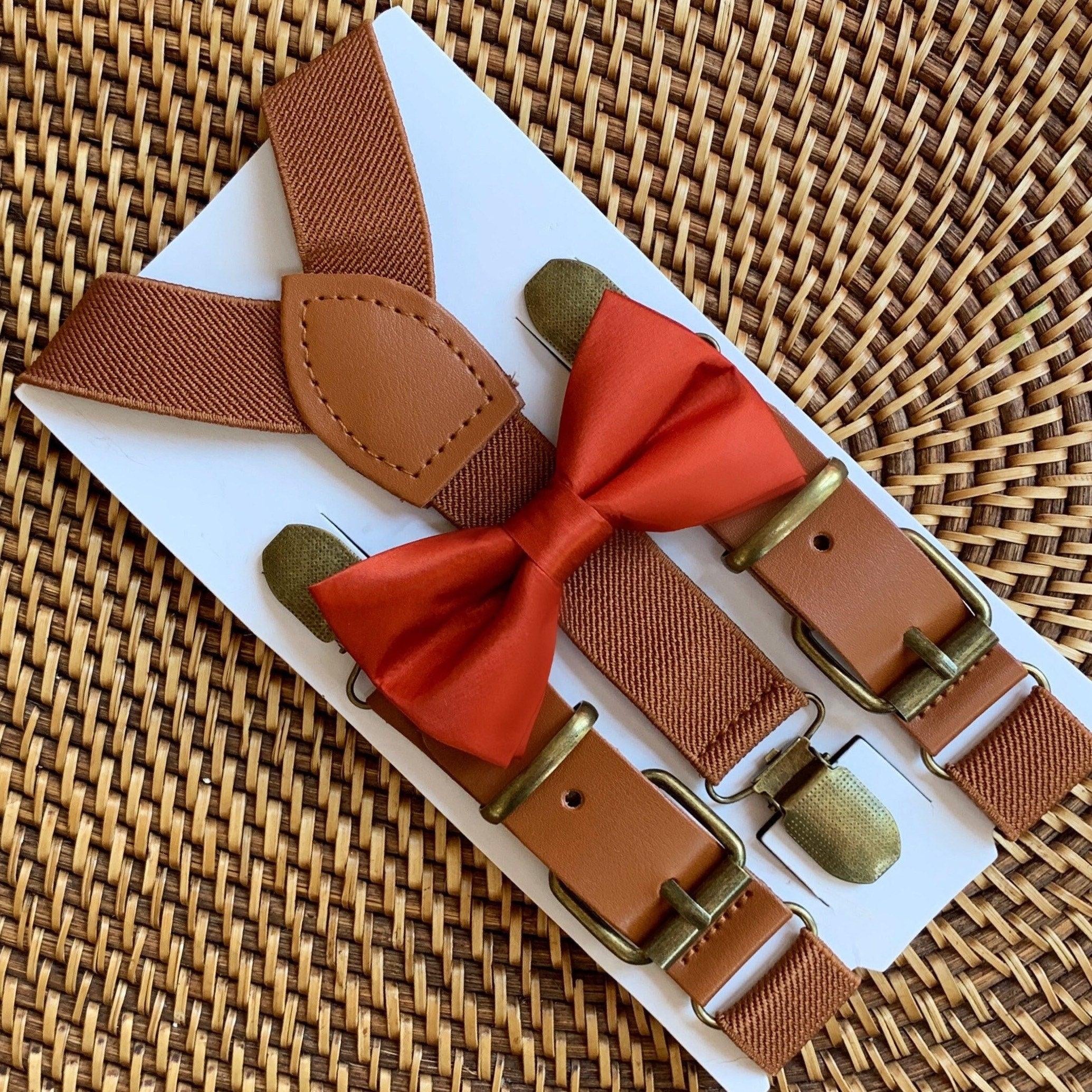 A set of burnt orange bow tie and brown elastic suspenders with a faux leather buckle, displayed on a white card.