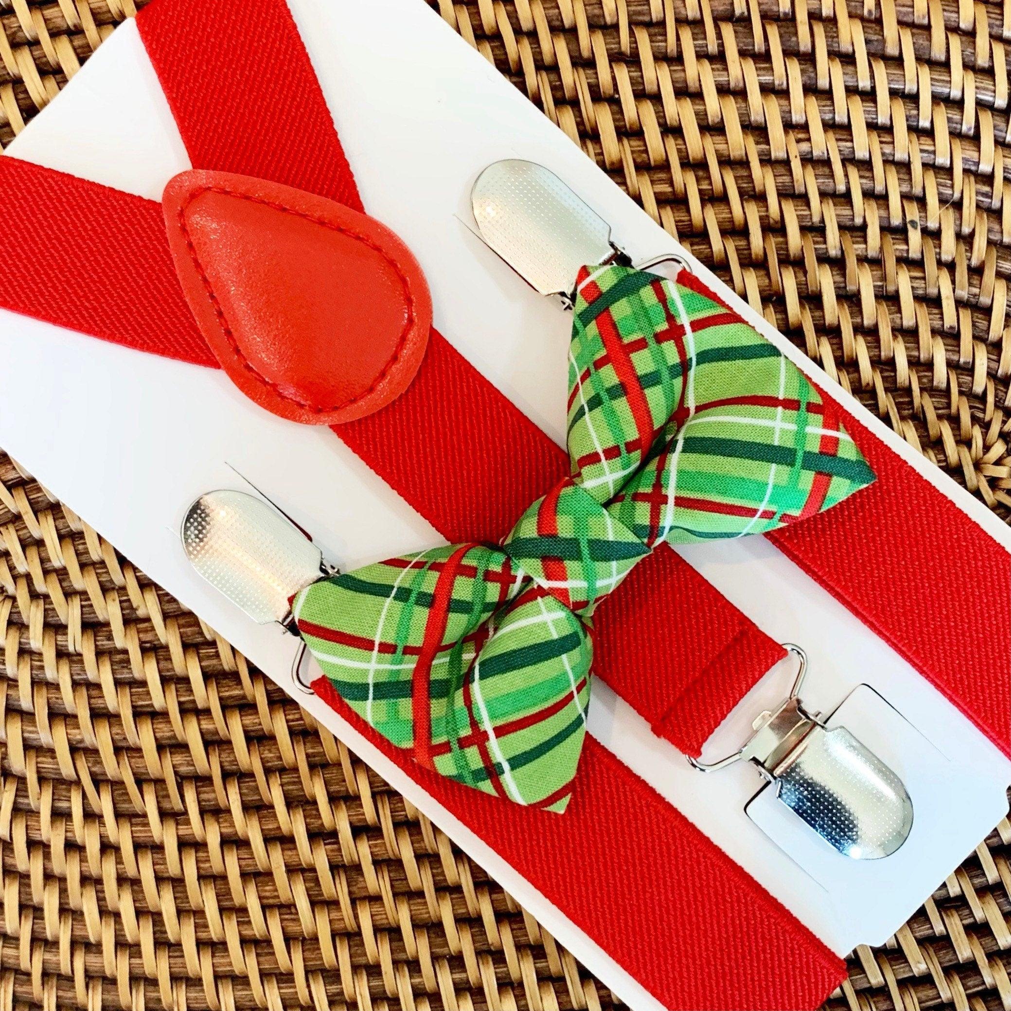 Close up of a red bow tie and red suspenders on a white card, with a green plaid bow tie and metal clips.