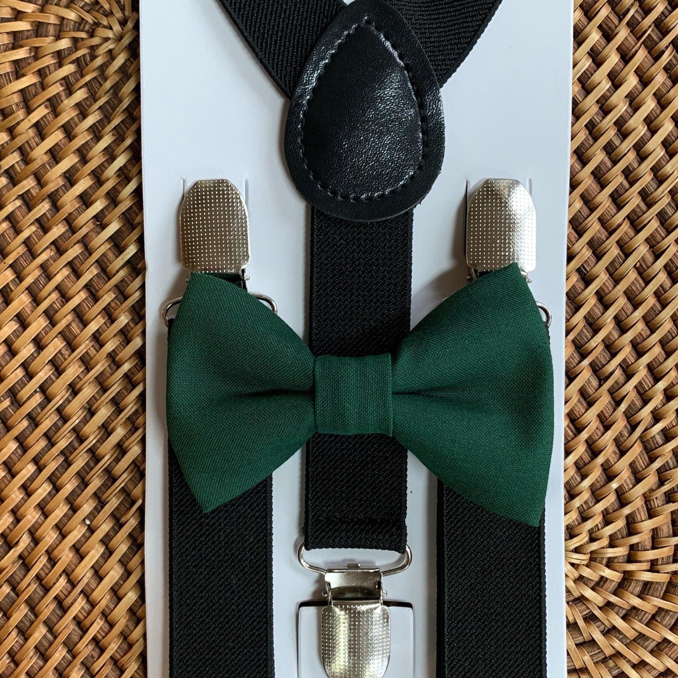 Close up of black suspenders with a green bow tie on a white display card