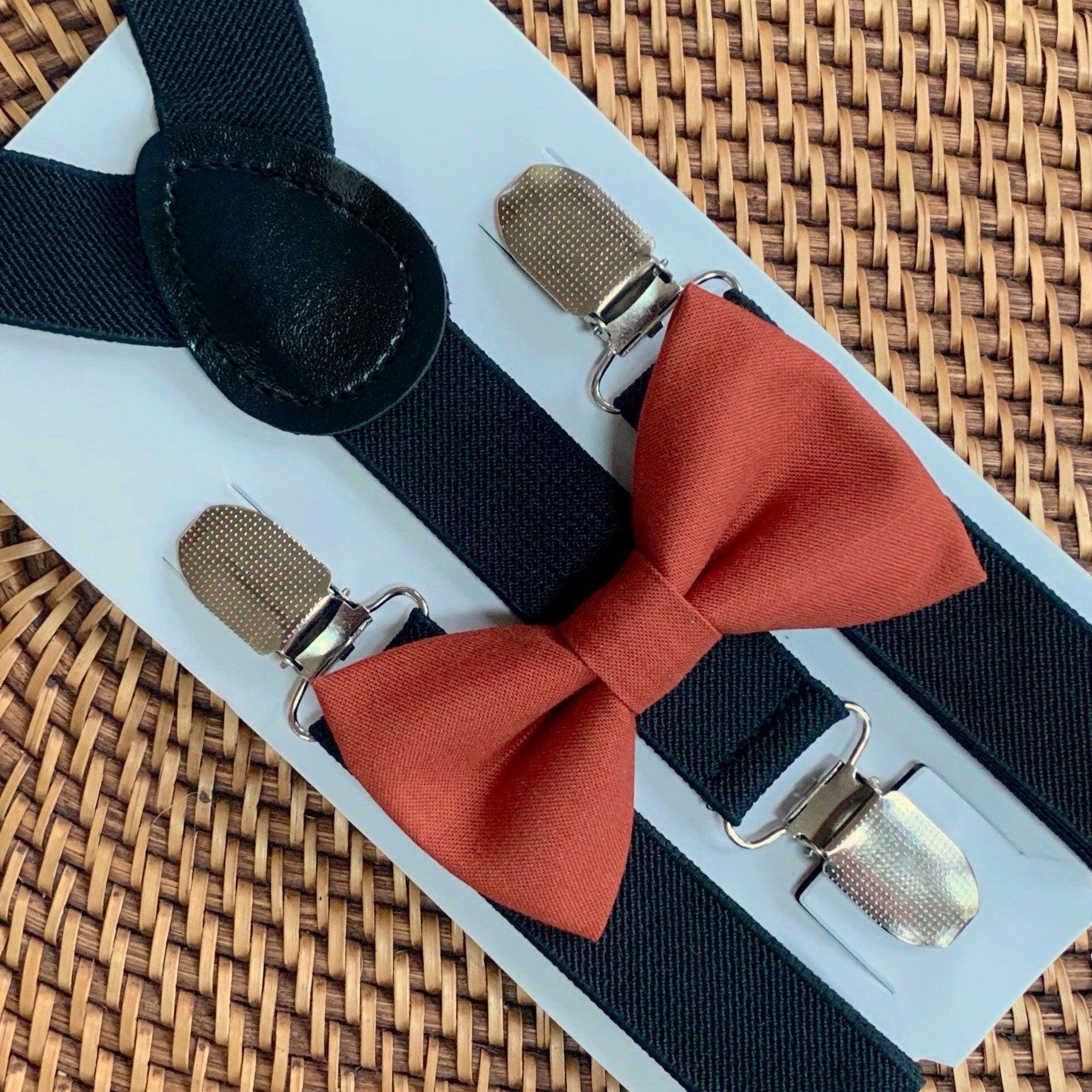 Terracotta bow tie with black suspenders displayed on a light blue backing against a woven wicker background.