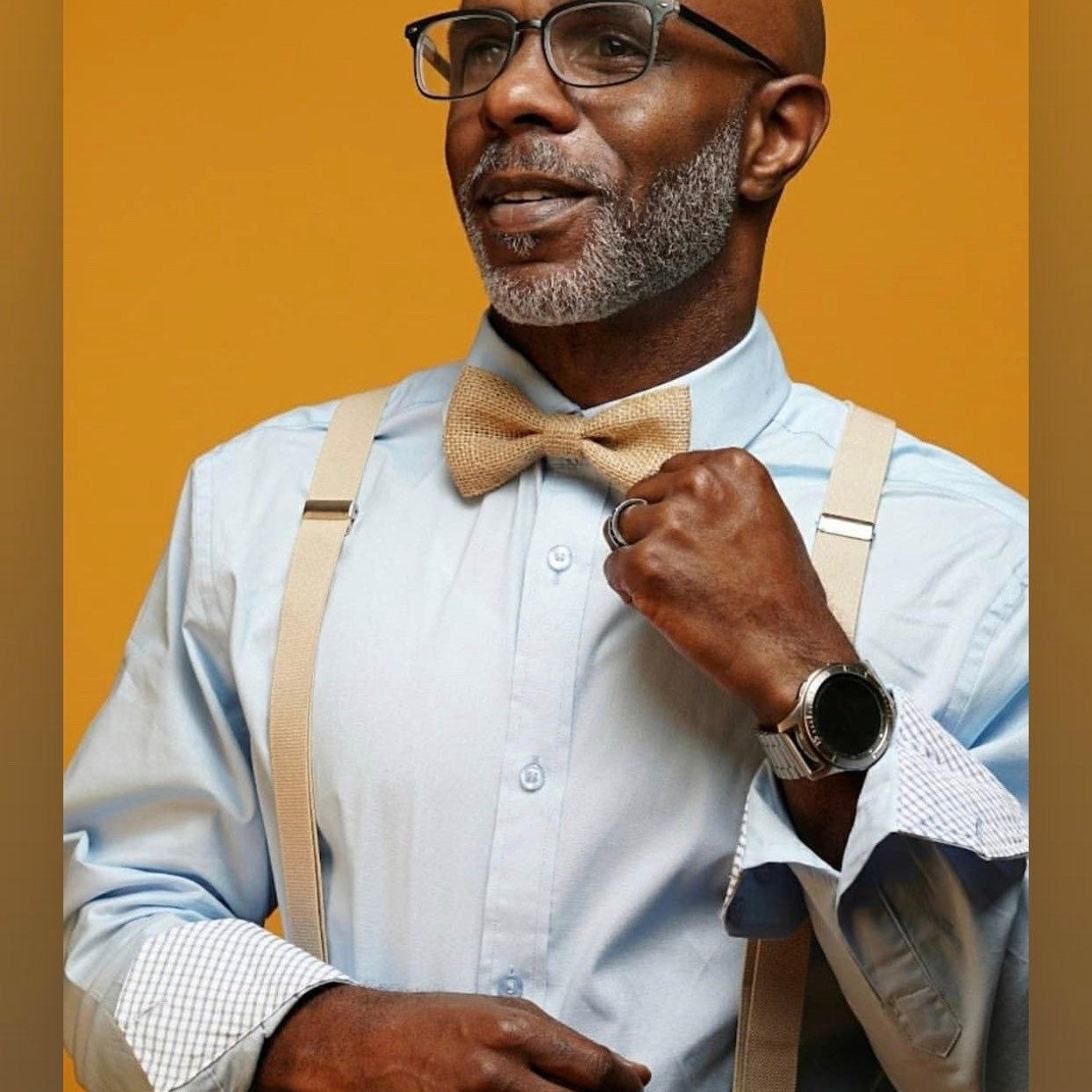 A handsome model wears a country chic burlap bow tie and rustic tan suspenders for a cowboy wedding.