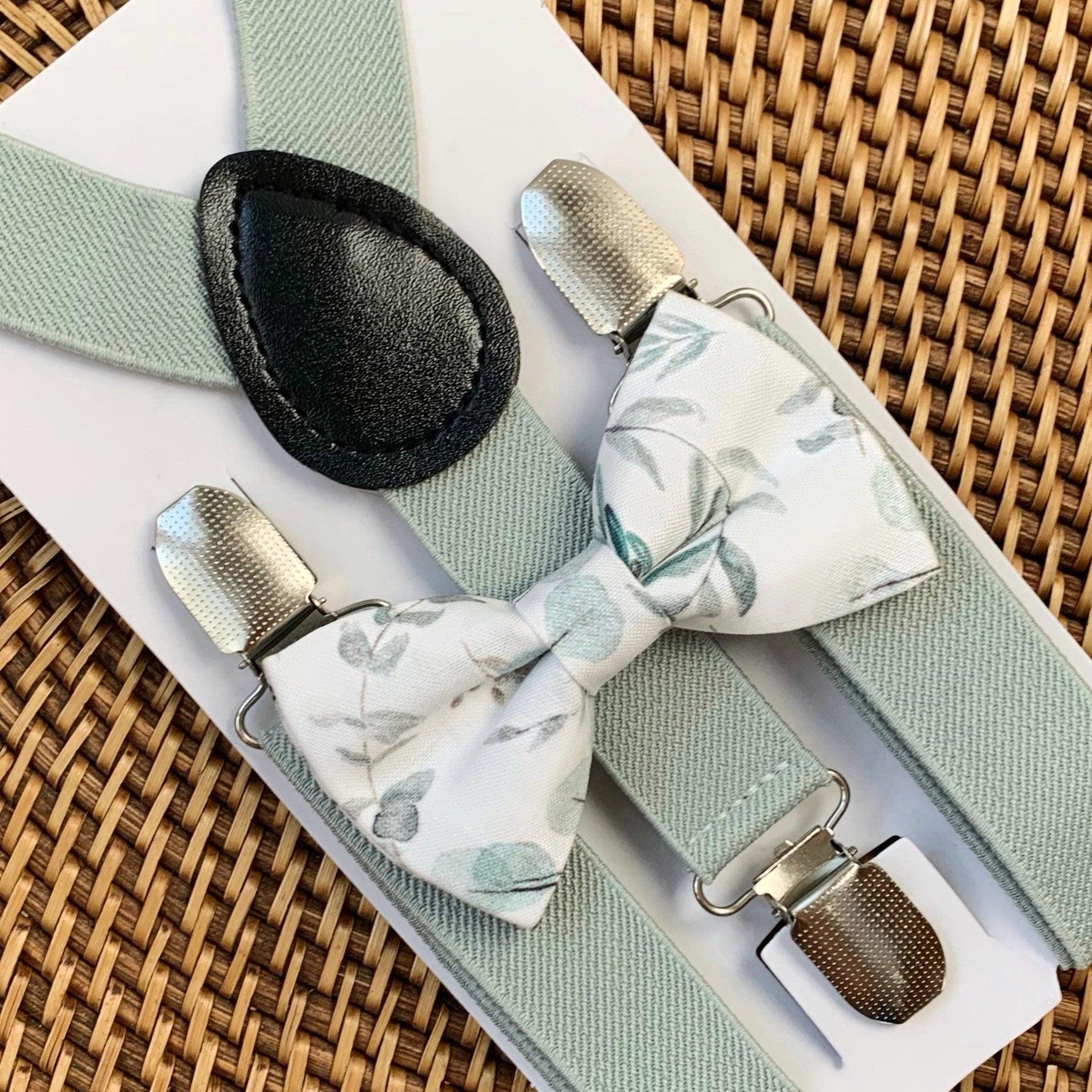 A set of sage green suspenders and a matching bow tie with a floral pattern displayed on a wooden surface.