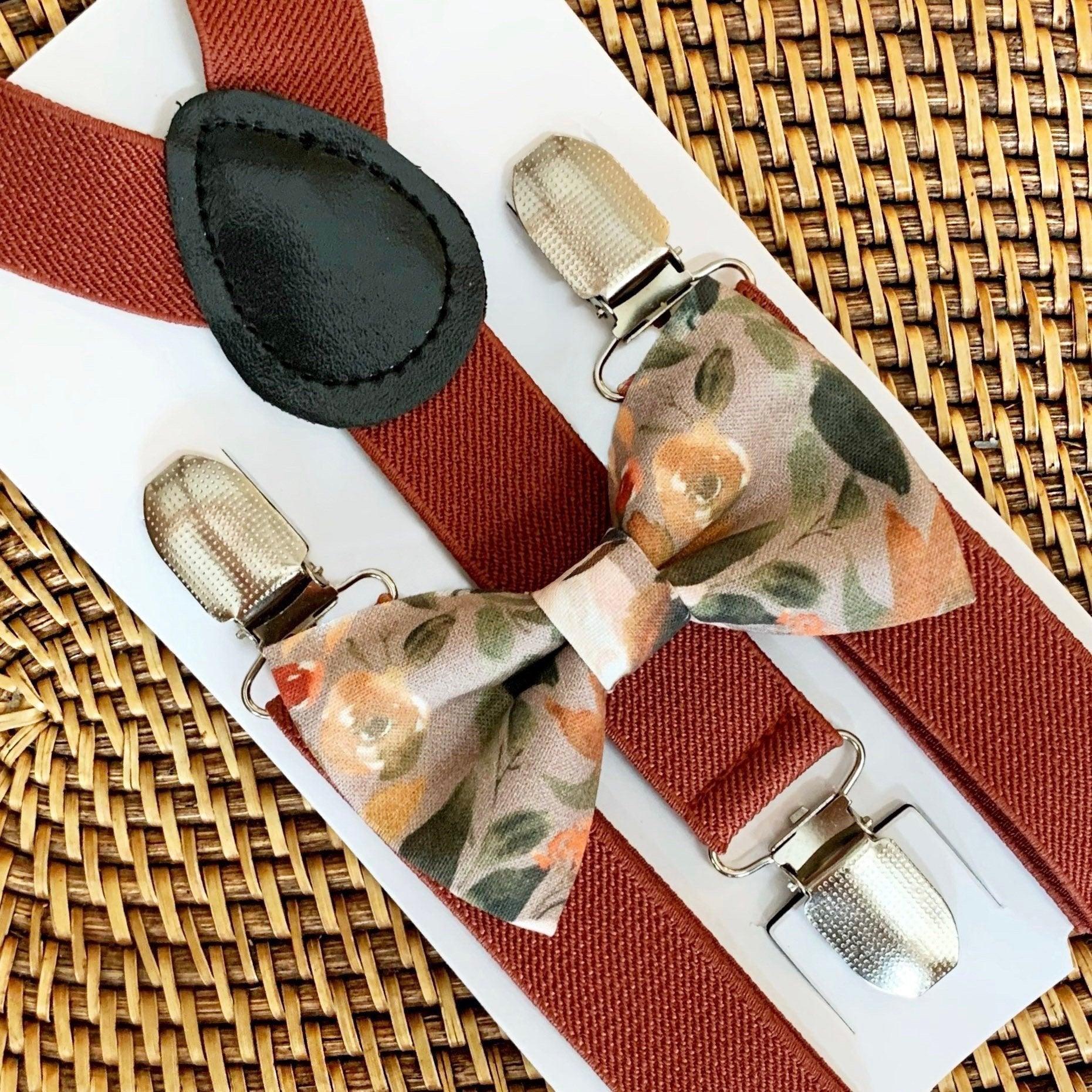 A set of terracotta colored elastic suspenders with a pre-tied autumn floral bow tie displayed on a wooden surface.