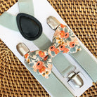 A set of peach Rifle Paper Co. bow tie and sage suspenders displayed on a wooden surface.