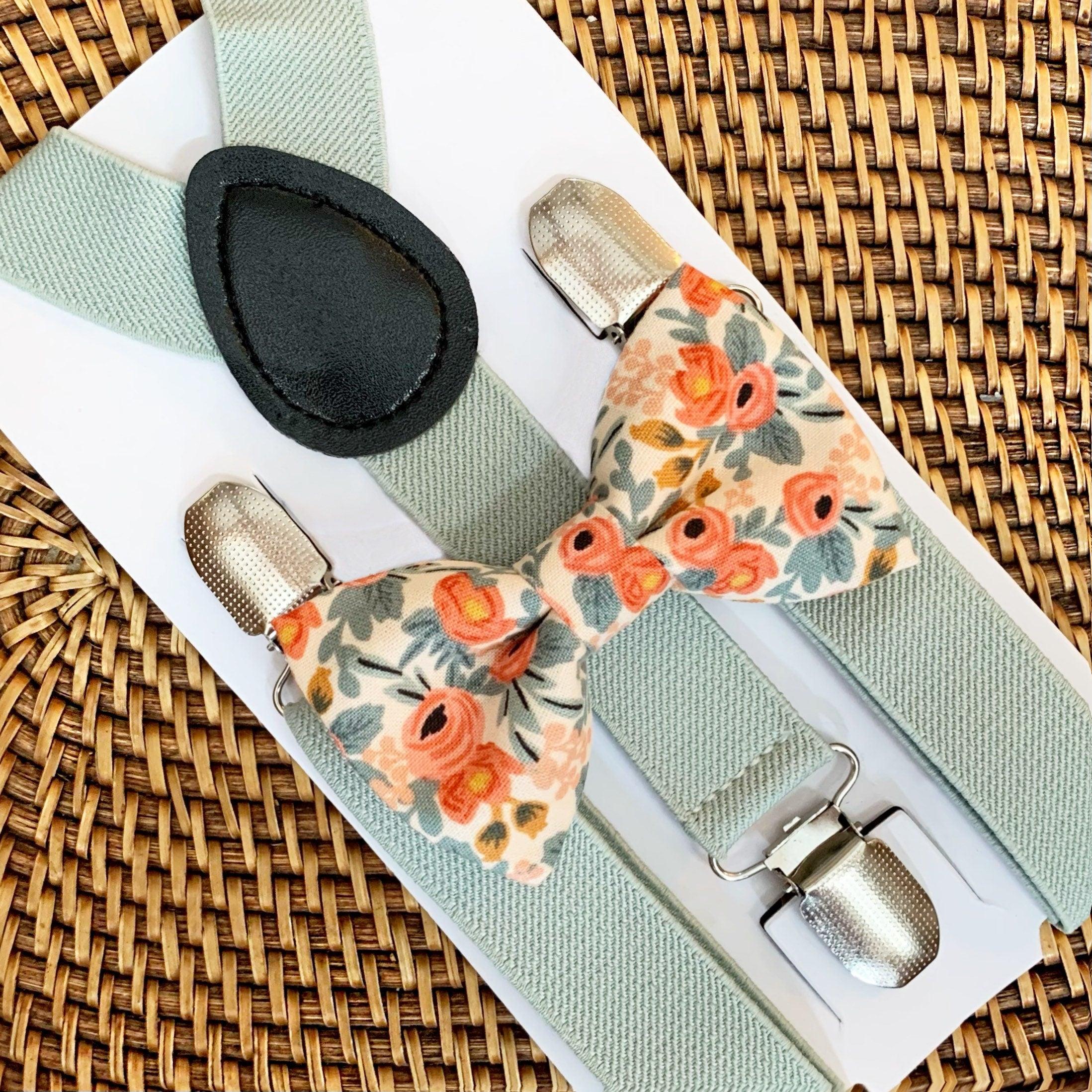 A set of peach Rifle Paper Co. bow tie and sage suspenders displayed on a wooden surface.