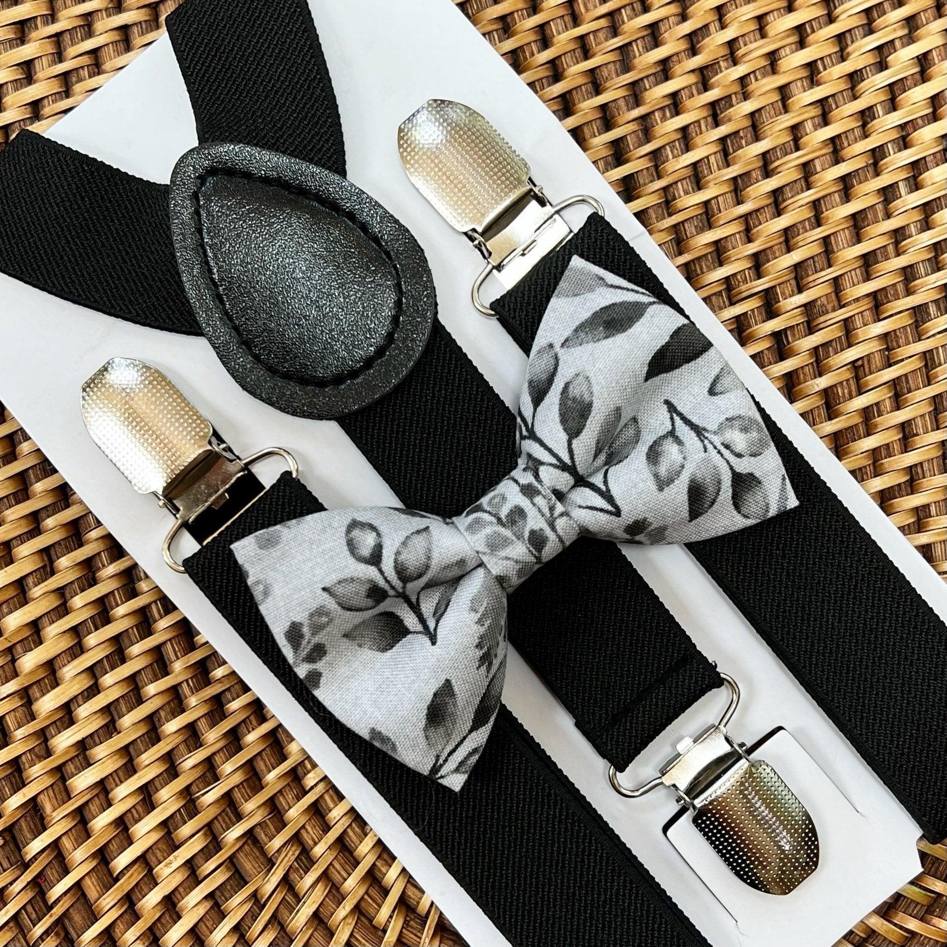 Grey floral bow tie with black suspenders on a white display card against a woven background.