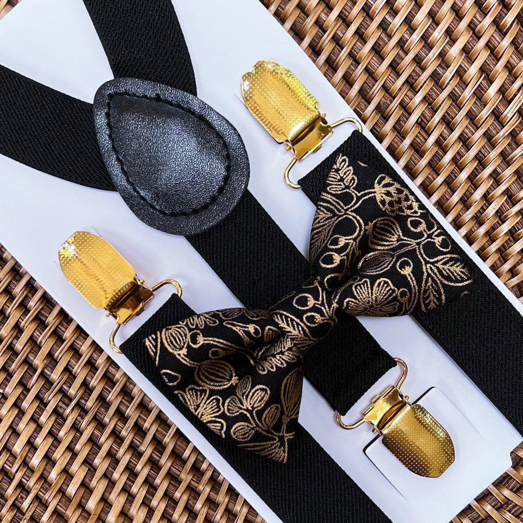 Close up of black bow tie and black and gold patterned suspenders on a white display card over a woven mat