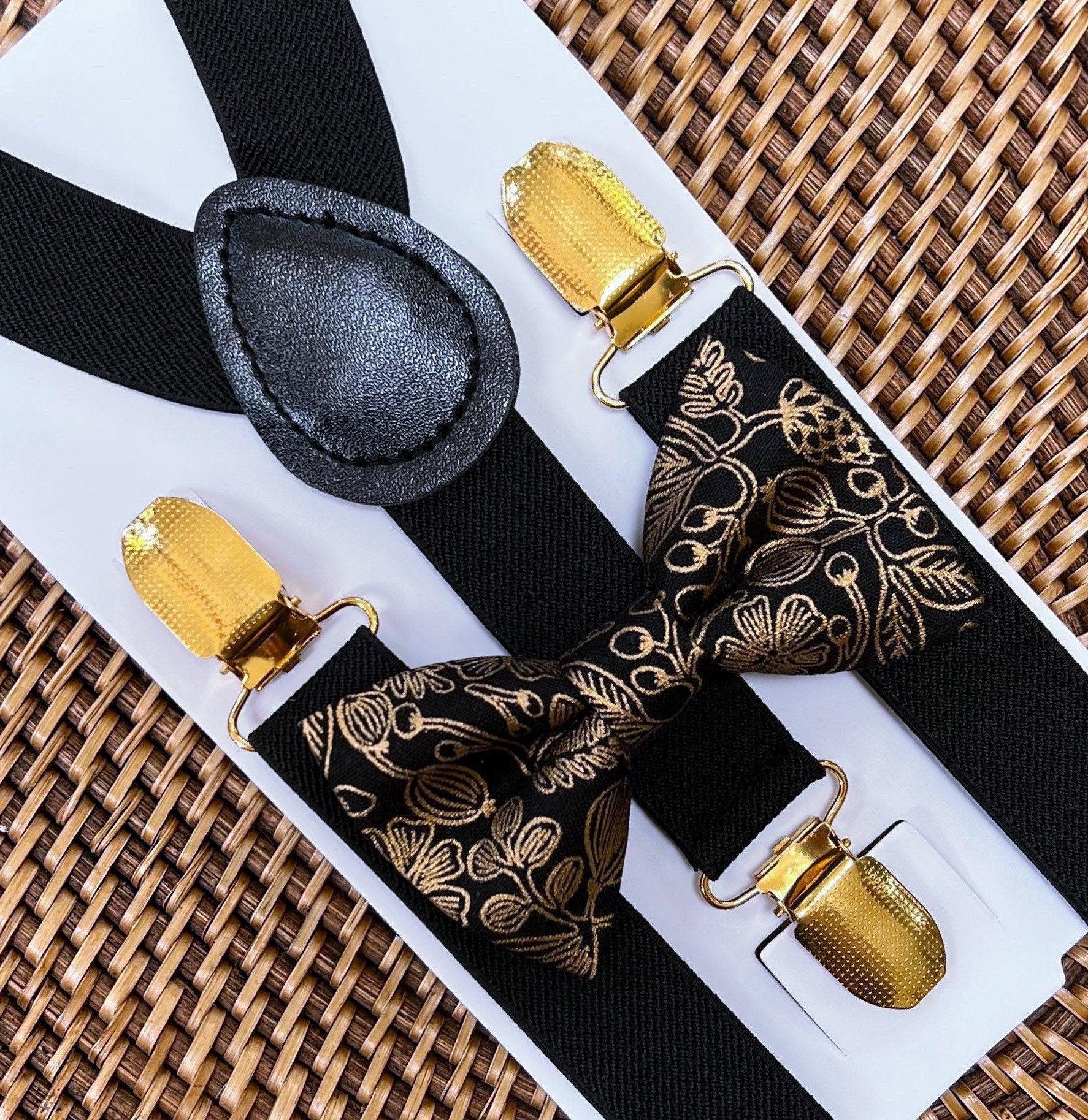 Close up of black bow tie and black and gold patterned suspenders on a white display card over a woven mat
