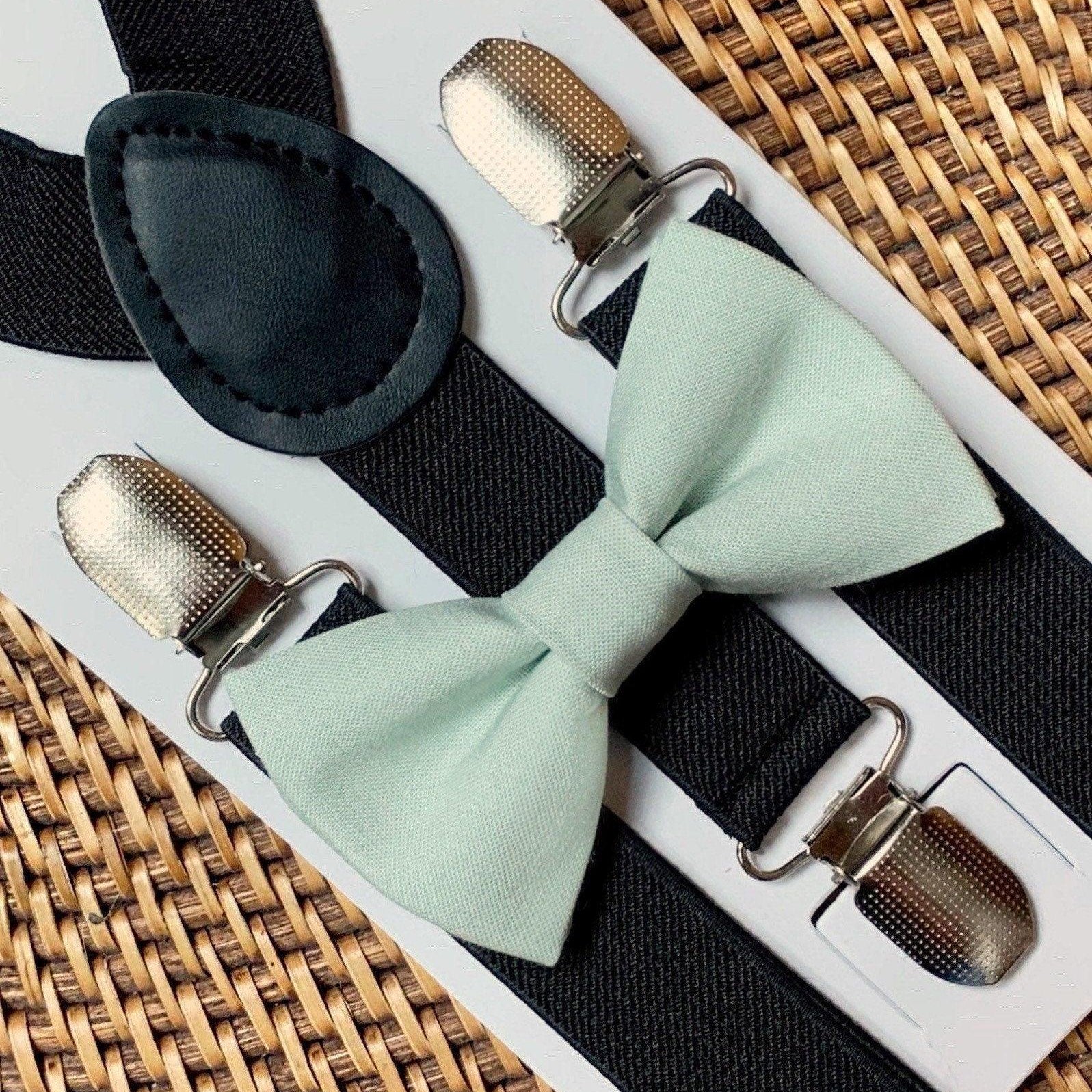 Sage bow tie with black suspenders displayed on a white card with metal clips in a close up shot