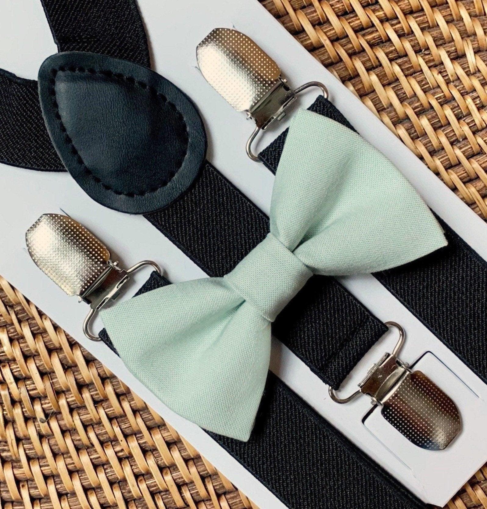 Sage bow tie with black suspenders displayed on a white card with metal clips in a close up shot