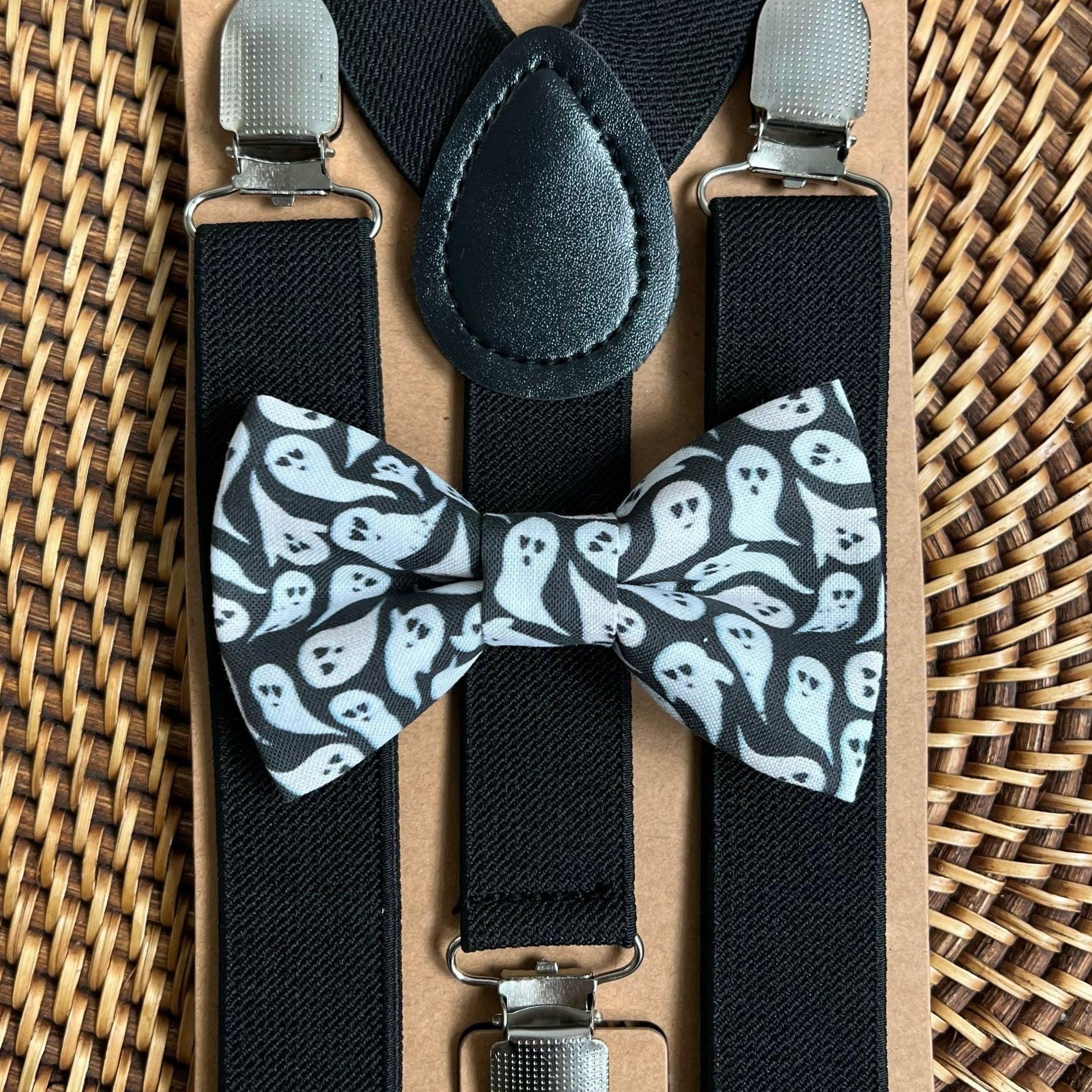 Front view of black suspenders with metal clips and ghost patterned bow tie on a cardboard backing.