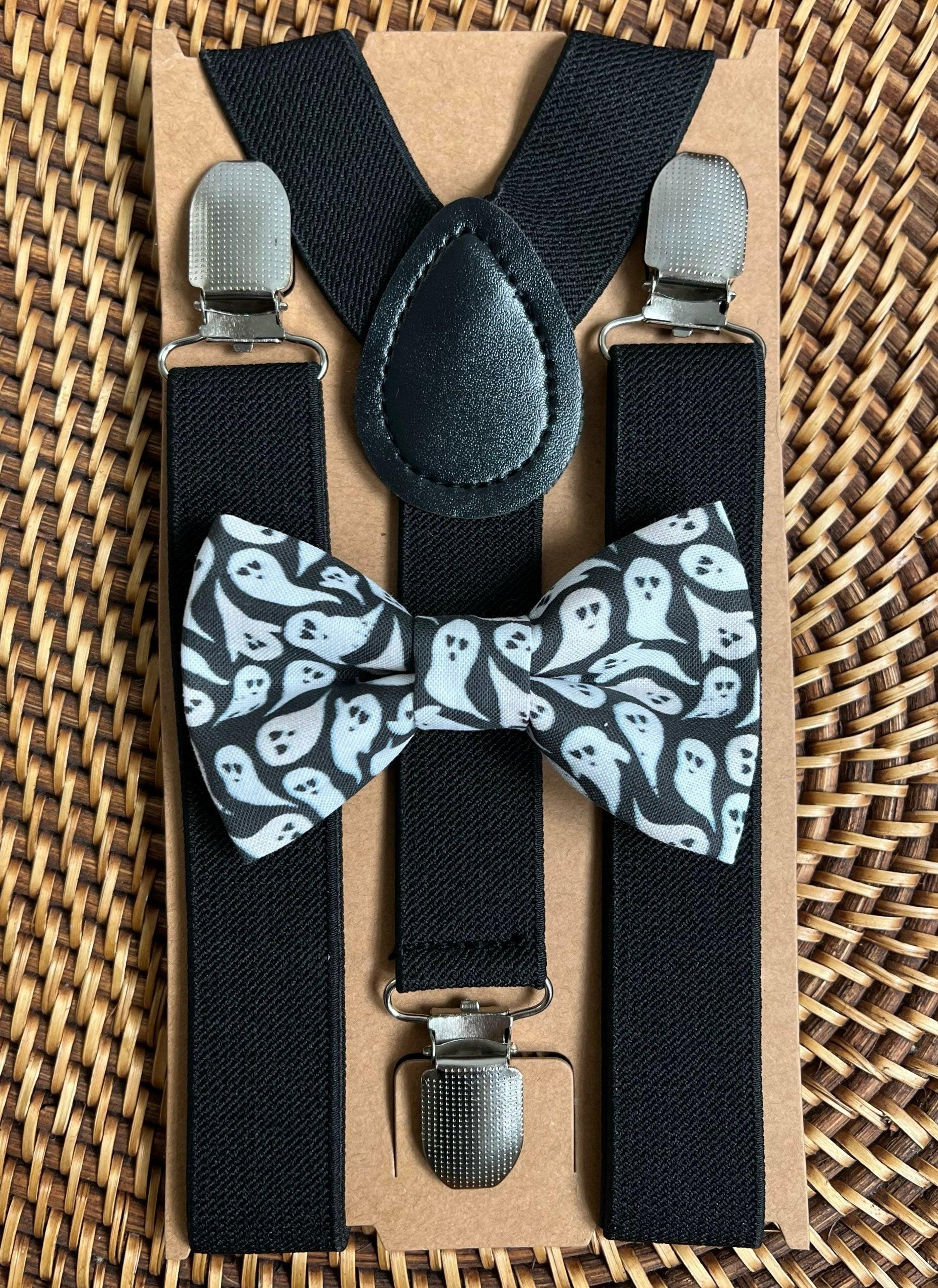 Front view of black suspenders with metal clips and ghost patterned bow tie on a cardboard backing.