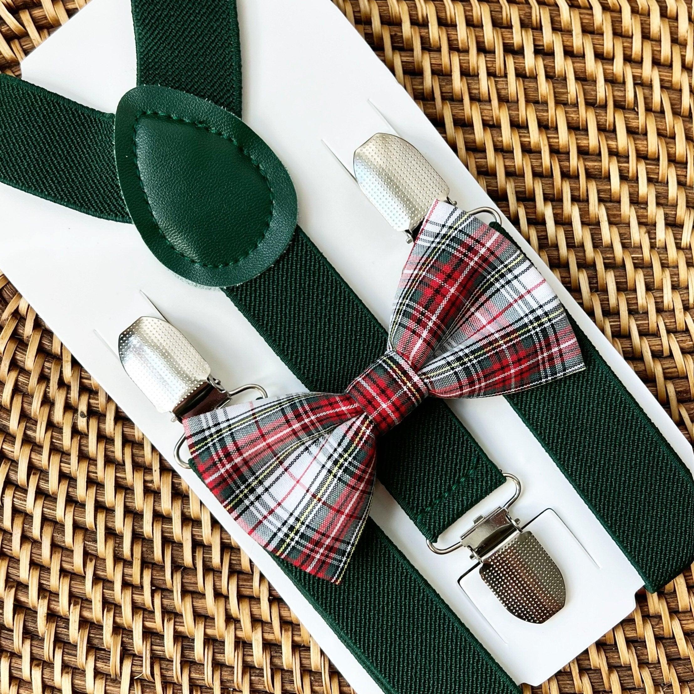 Green suspenders with a dark green textured strap and a red green plaid bow tie on a white card against a wicker background