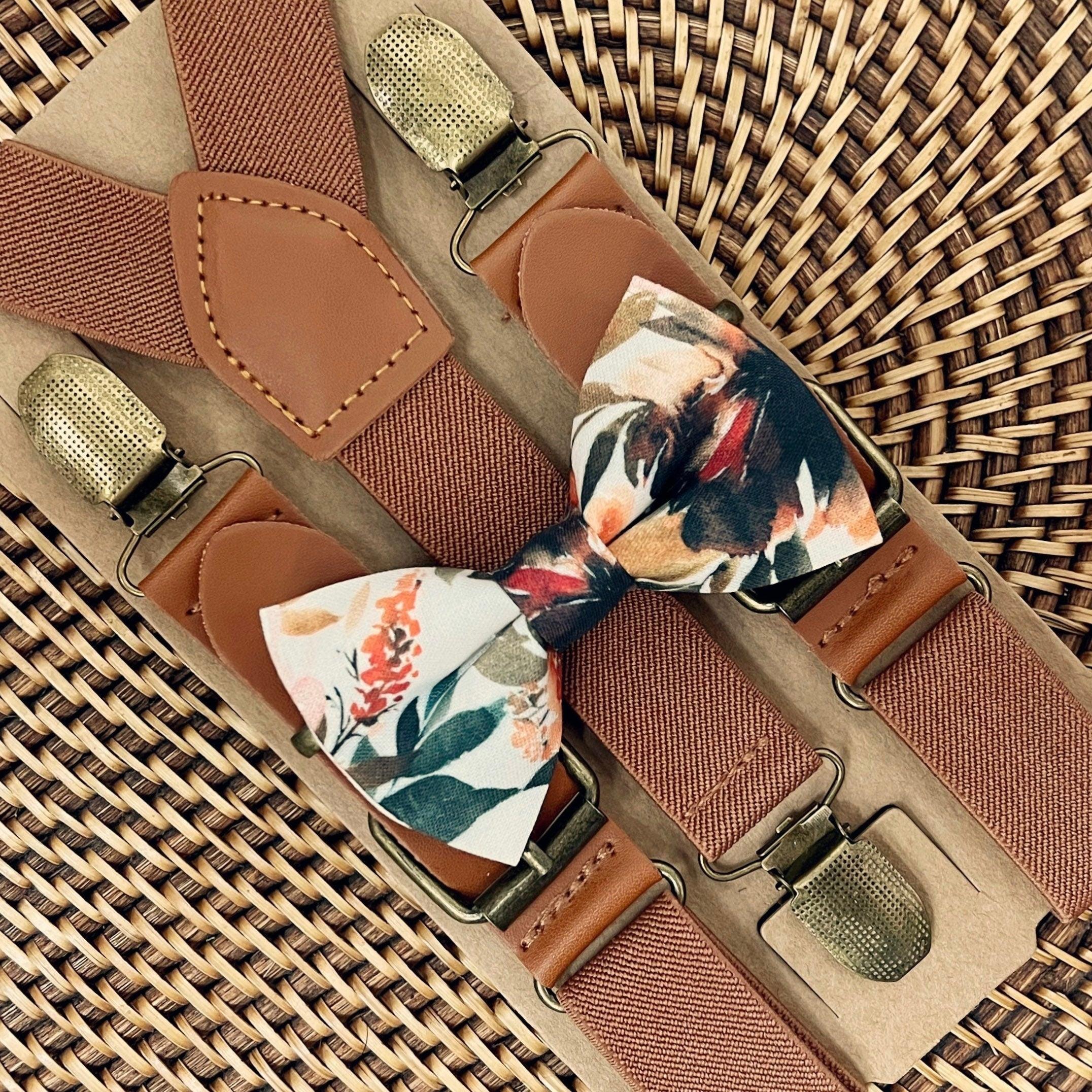 A set of brown vegan leather suspenders with ivory terracotta floral bow tie attached to them, displayed on a woven background.
