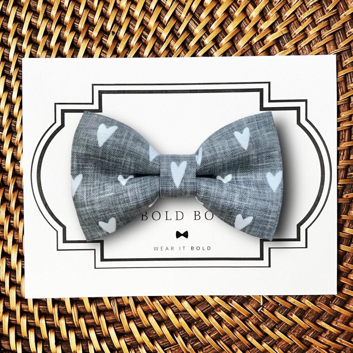 Gray Valentines day dog bow tie with heart patterns on a white card with 'Bold Bow' branding, placed on a woven surface.