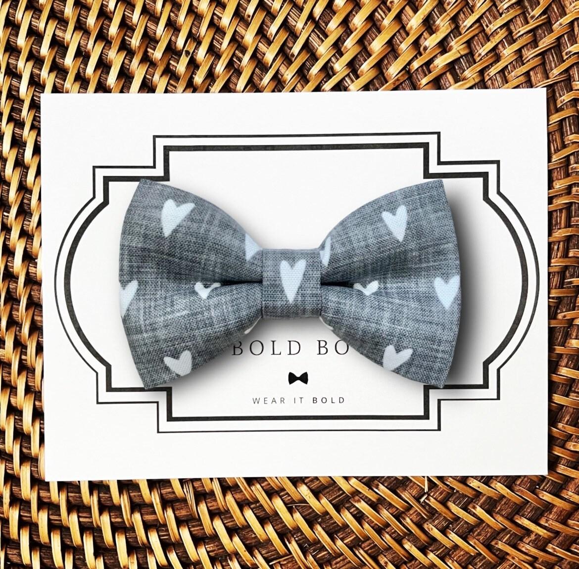 Gray Valentines day dog bow tie with heart patterns on a white card with 'Bold Bow' branding, placed on a woven surface.