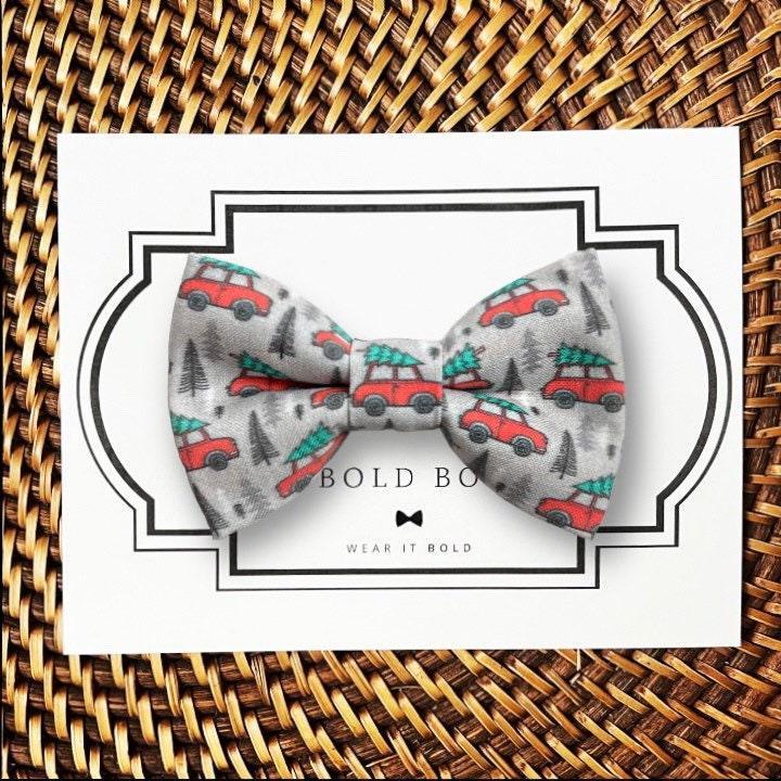Product graphic showcasing the back of a pre-tied bow tie in a red and black buffalo plaid pattern, resting on a rustic wood surface. Two black elastic loops are attached to the center knot to slide onto a pet collar. Overlay text reads: Back of Bow Tie (may not be actual bow tie in listing).