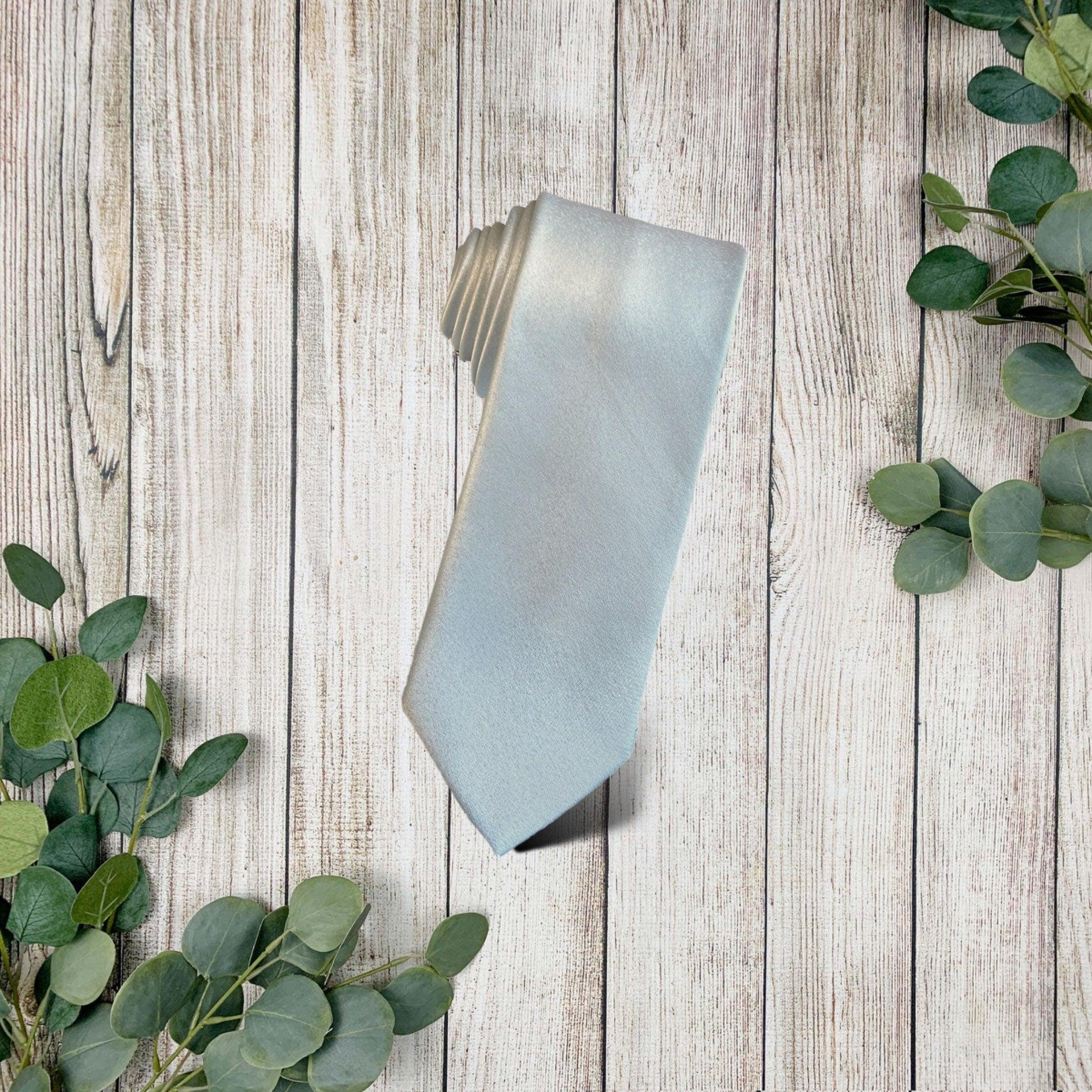 Folded Cinderella blue necktie on a weathered wooden surface with eucalyptus sprigs.