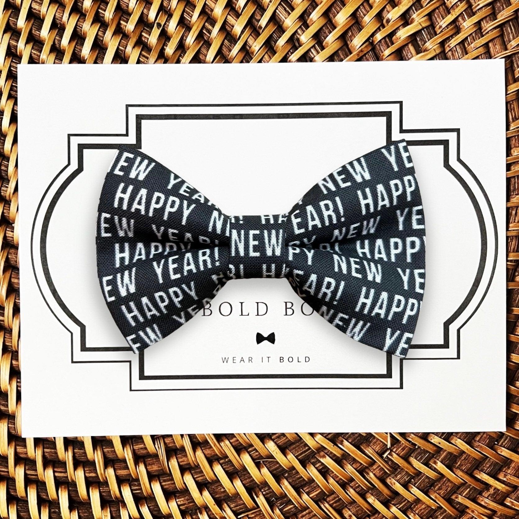 Product graphic showcasing the back of a pre-tied bow tie in a red and black buffalo plaid pattern, resting on a rustic wood surface. Two black elastic loops are attached to the center knot to slide onto a pet collar. Overlay text reads: Back of Bow Tie (may not be actual bow tie in listing).
