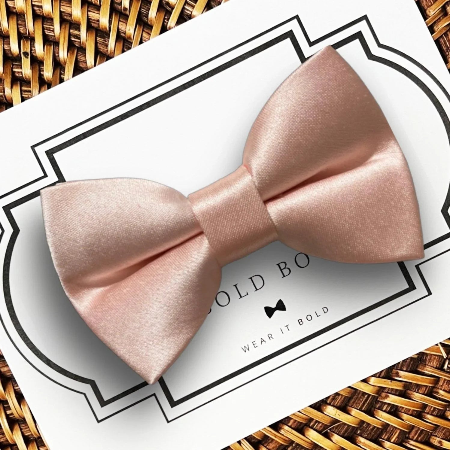 Close up of a blush satin bow on a white decorative card against a woven background