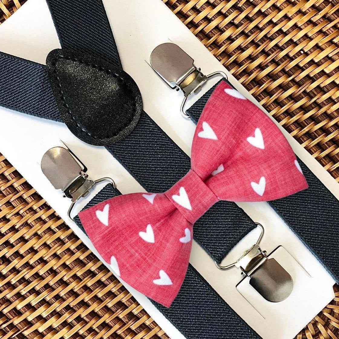 Red hearts bow tie with dark grey suspenders set on a textured surface