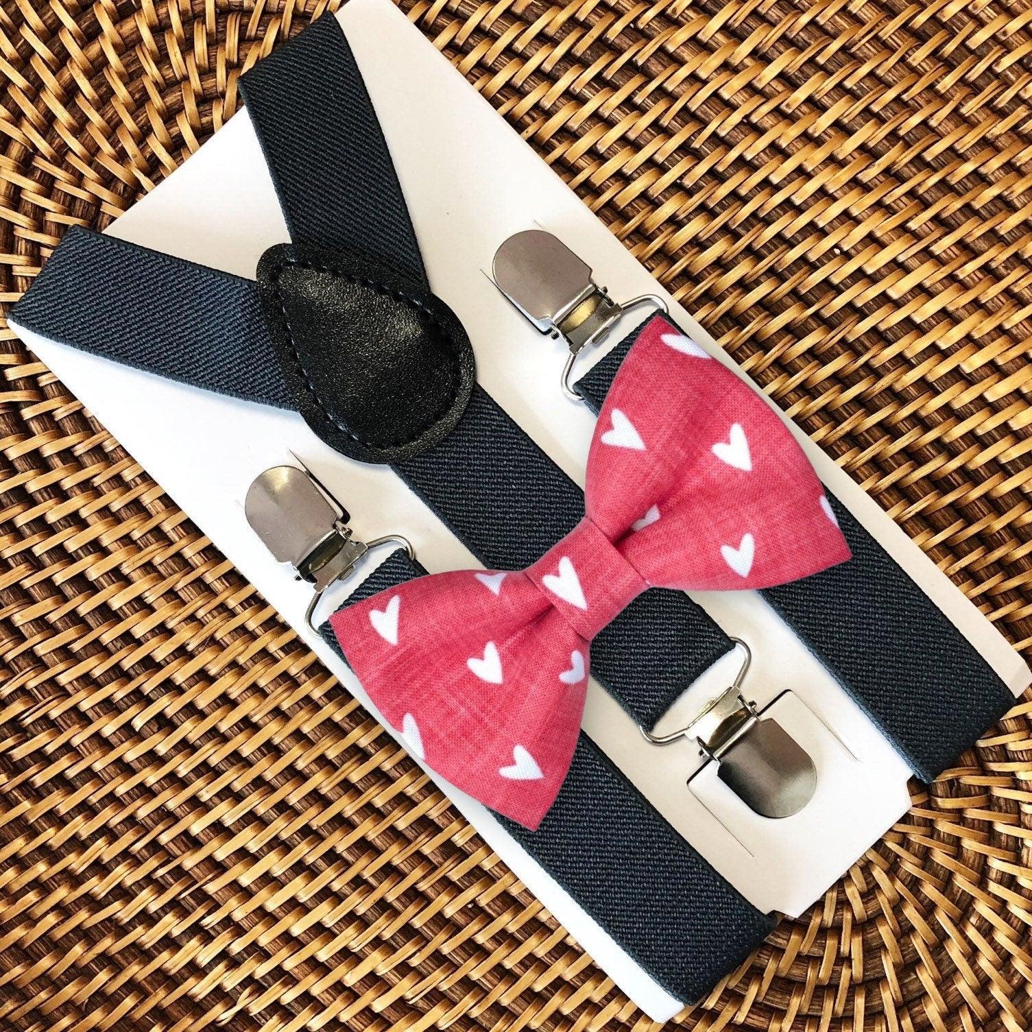 Dark grey suspenders with a round black leather patch paired with a pink heart patterned bow tie on a white display card