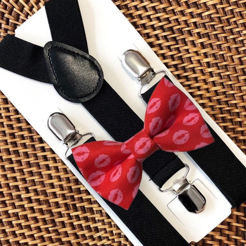 Black suspenders with a red bow tie featuring pink kiss marks on a woven surface for Valentine's Day.