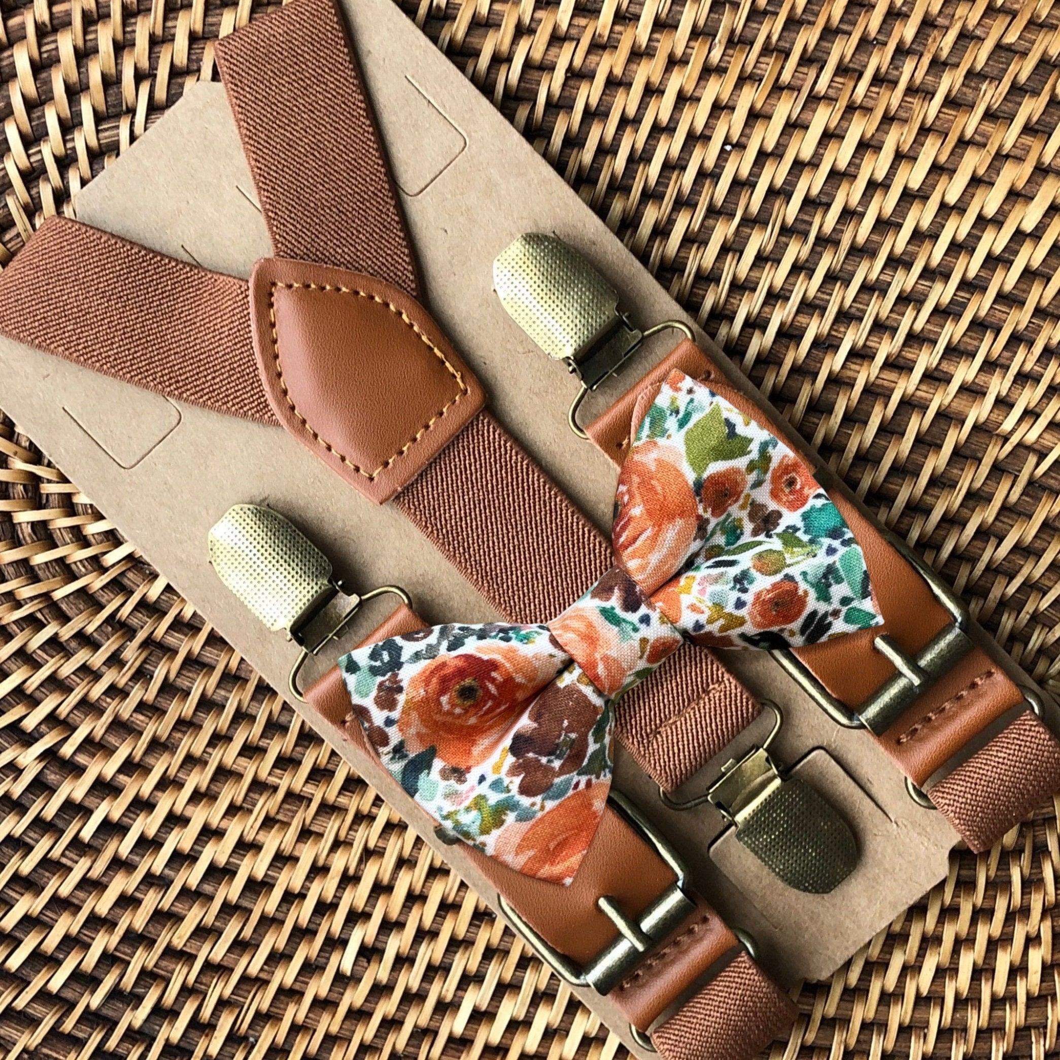 A set of brown suspenders with an orange floral bow tie on a wooden surface.