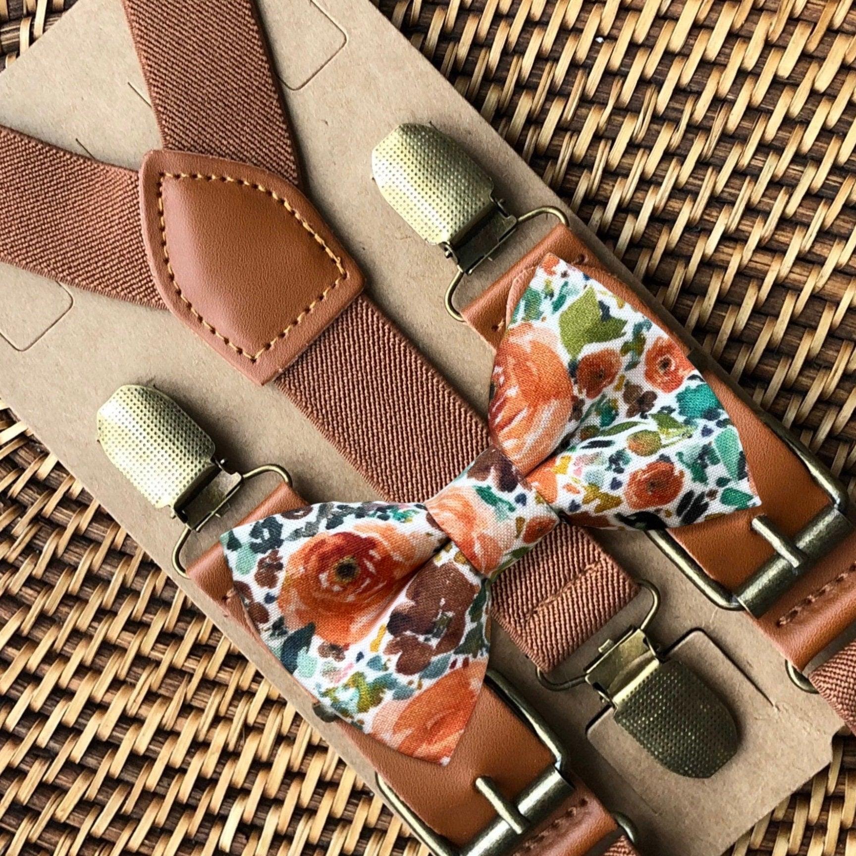 A set of brown suspenders with an orange floral bow tie on a wooden surface.