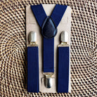 Navy blue suspenders with silver clips on a cardboard backing against a woven background