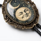 A decorative pendant featuring a moon and crescent symbol, with a smiling face in the center, is displayed on a black braided cord.