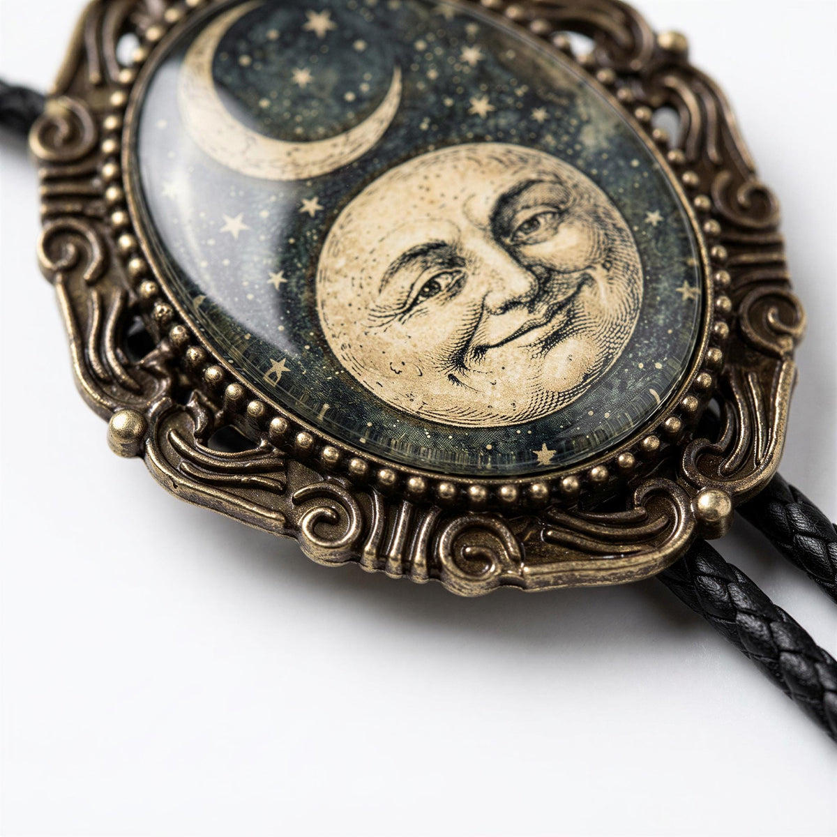 A decorative pendant featuring a moon and crescent symbol, with a smiling face in the center, is displayed on a black braided cord.