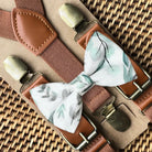 Floral bow tie with brown suspenders on a woven surface for groomsmen and ring bearers for wedding.