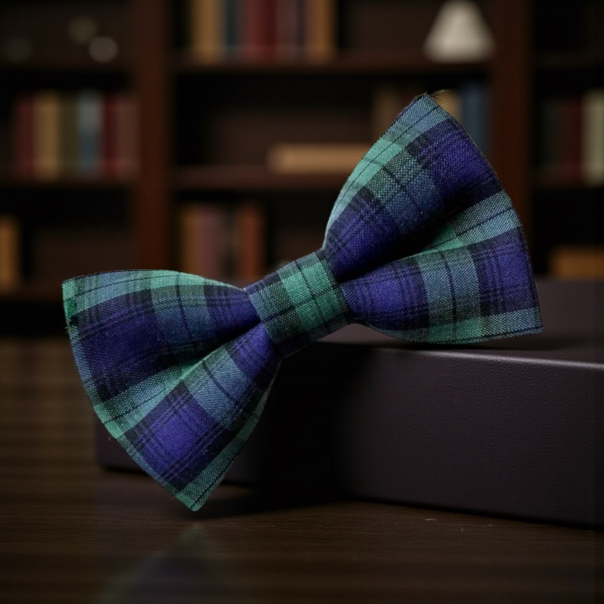 Plaid bow tie on a dark surface with a blurred bookshelf background