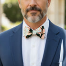 Groomsman wearing a pink floral bow tie and a blue suit at a wedding.