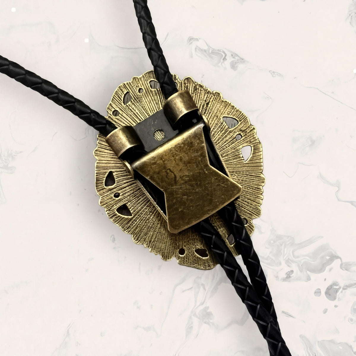 A close-up view of a decorative metal piece with a black braided cord attached to it, resting on a marble surface.