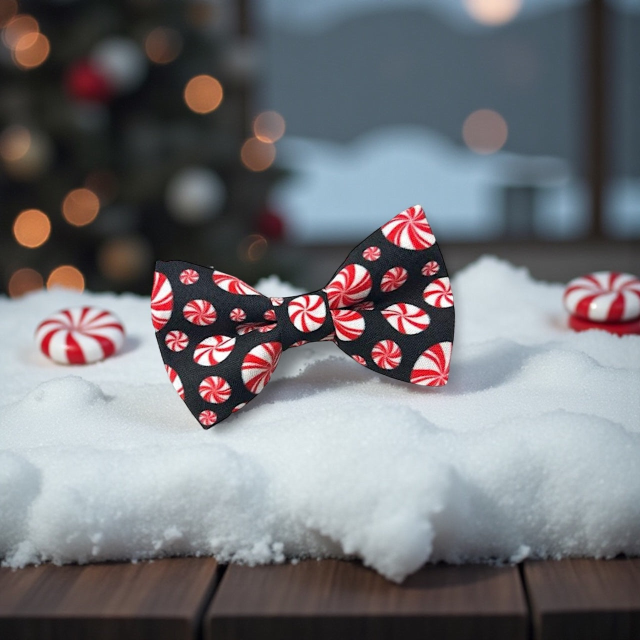 Bow tie with peppermint candy pattern on a snowy surface with blurred Christmas tree in the background