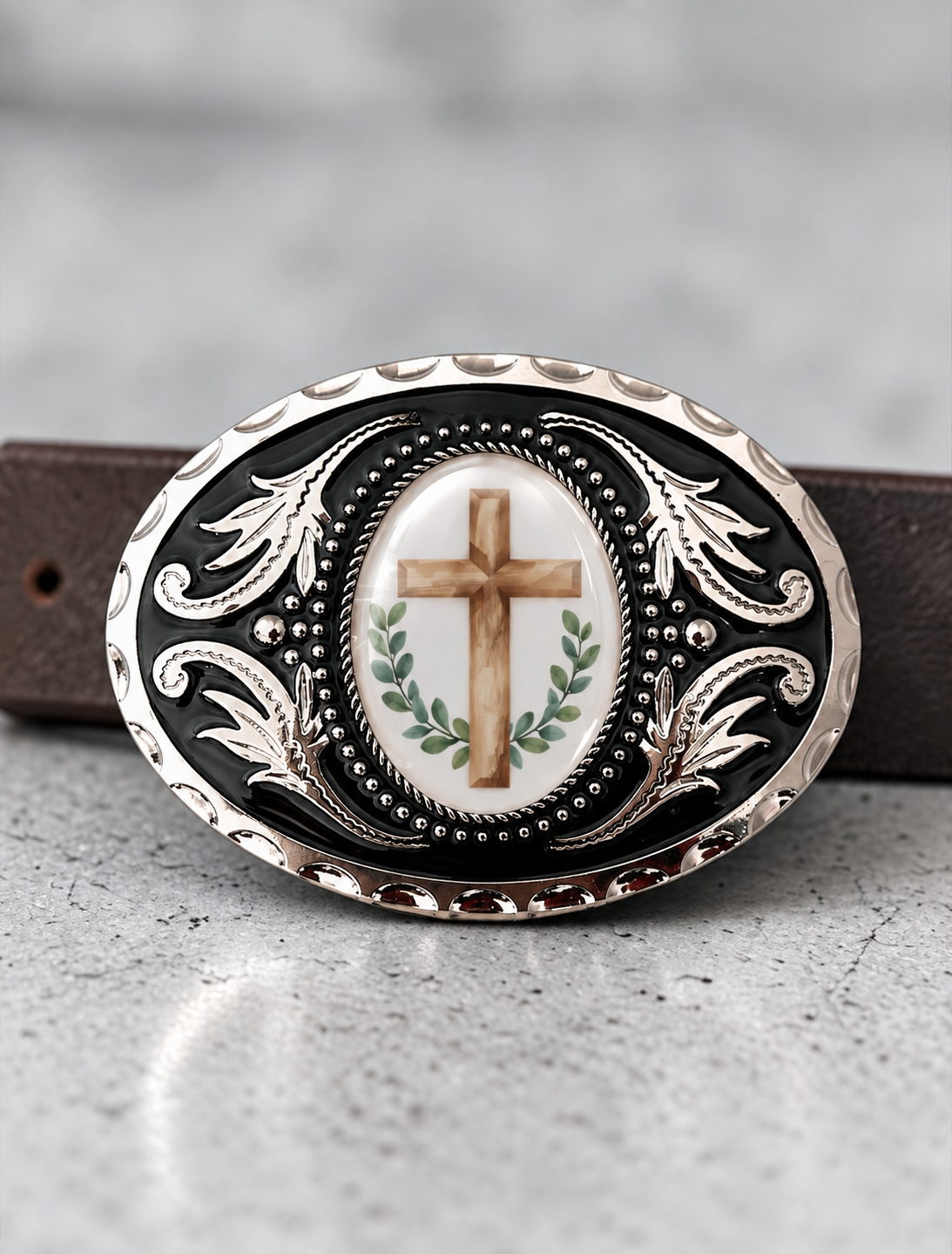 A decorative oval-shaped belt buckle with a cross and laurel wreath design.