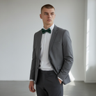 Man wearing a gray suit with a green bow tie in a minimalistic setting