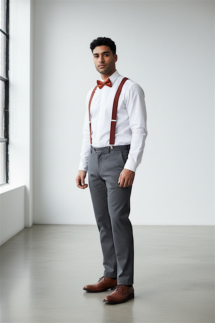 Man wearing a white shirt, gray pants, burnt orange bow tie, terracotta suspenders, and brown shoes as a groomsman in a wedding.