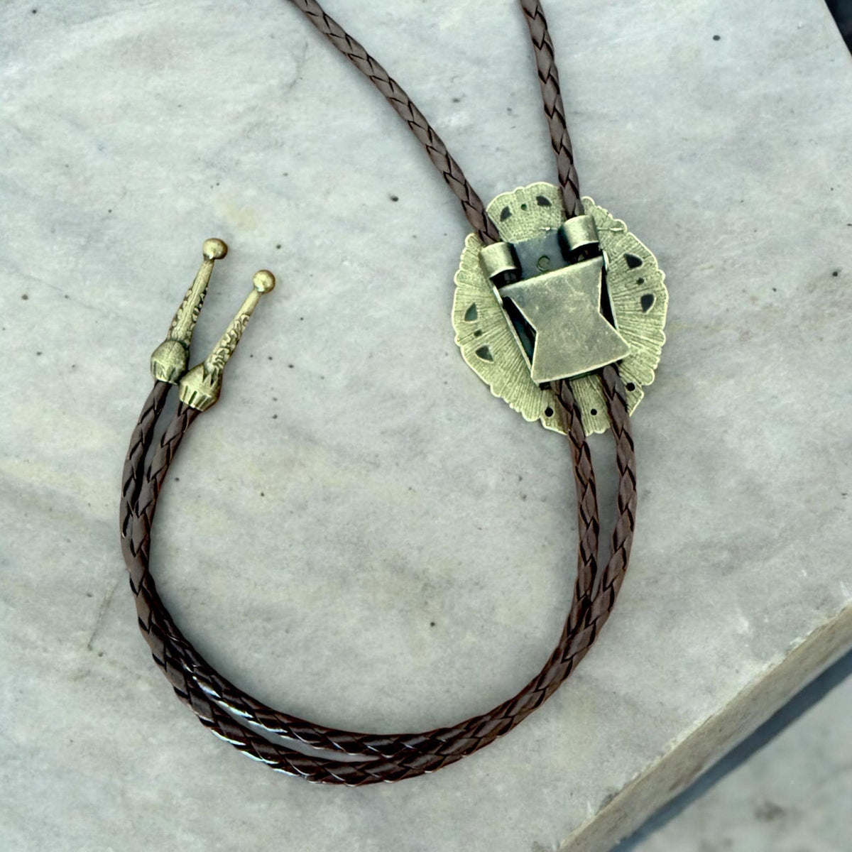 A brown braided leather bobby pin with a metal clasp and decorative elements is shown on a gray surface.