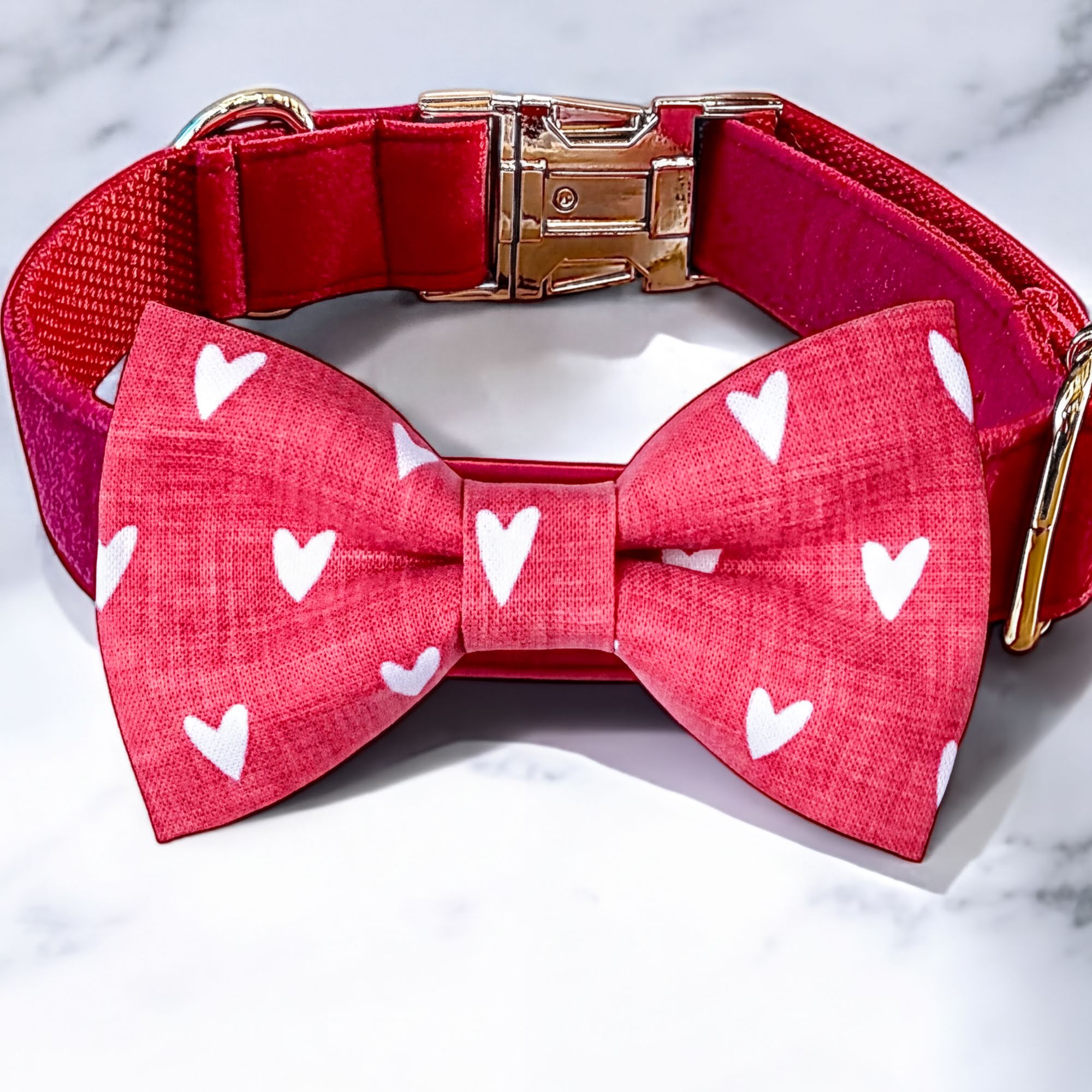 Red dog collar with a matching dog bow tie featuring white heart patterns on a marble background.