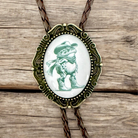 Bolo tie with a frog wearing a cowboy hat on an oval pendant, set against a wooden background.