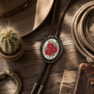 Black braided vegan leather cord bolo tie with decorative antique brass metal tips attached to a large glass dome holiday poinsettia cabochon.