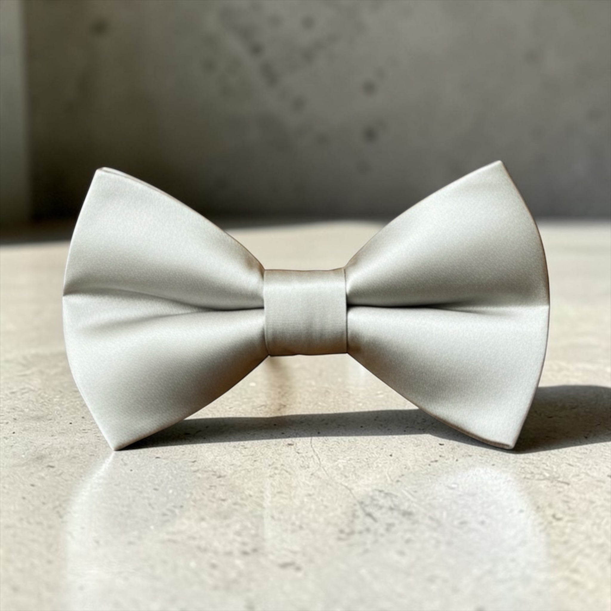 Silver bow tie for men, boys and groomsmen on a textured surface with a neutral background