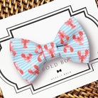 Dog Bow tie with red lobster pattern on a light blue background, displayed on a surface with 'Bold Bow' branding.