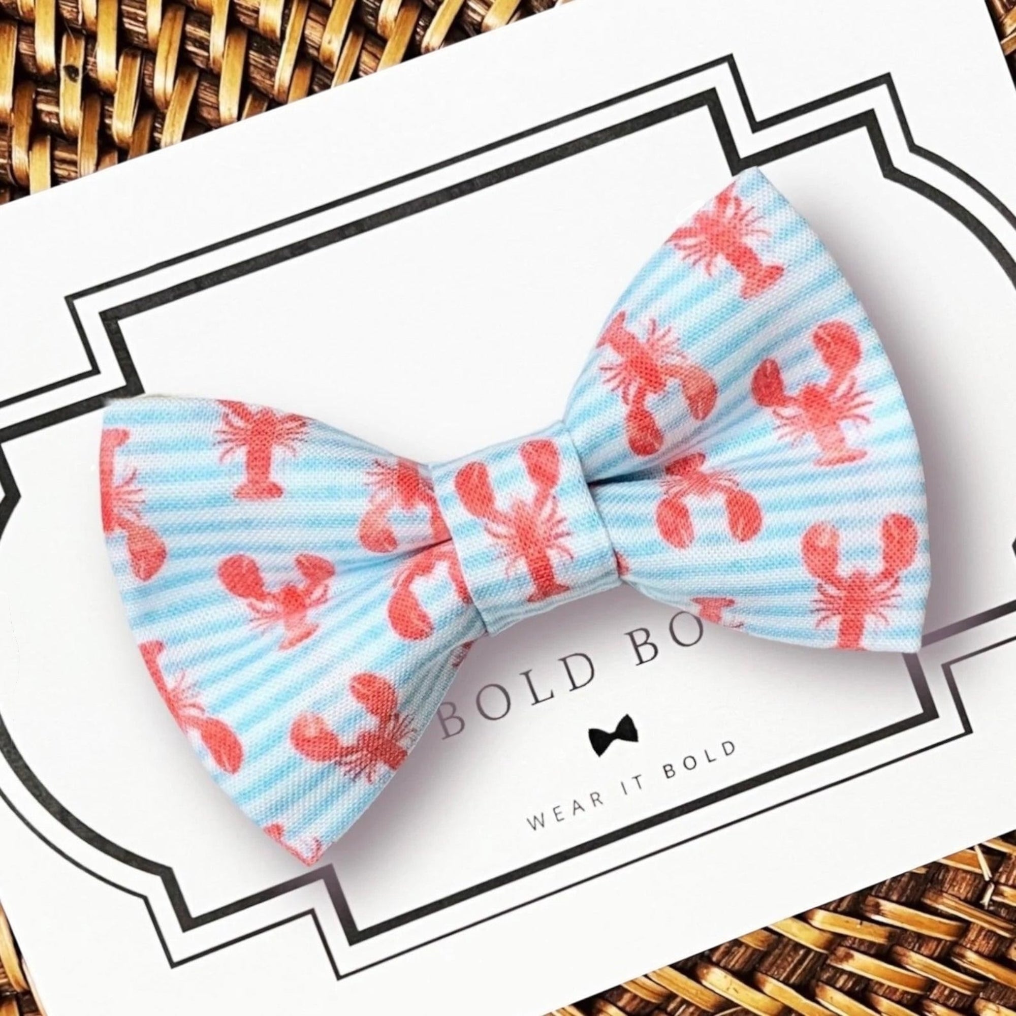 Dog Bow tie with red lobster pattern on a light blue background, displayed on a surface with 'Bold Bow' branding.
